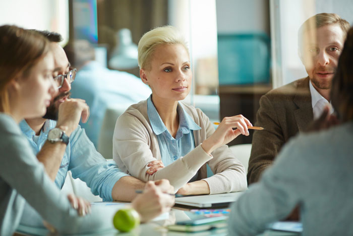 Office meeting showing employees discussing work, illustrating themes of employee sidelining and corporate spying on staff.