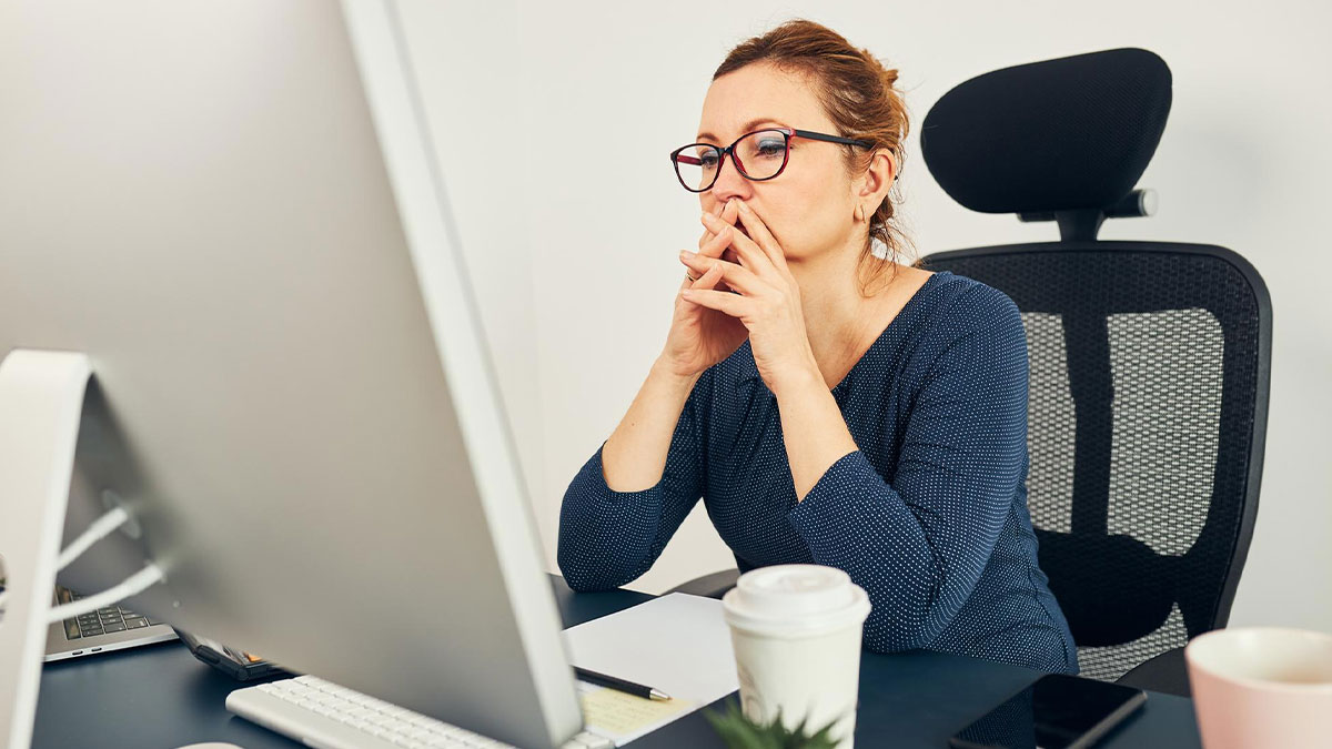 Female employee in glasses looking concerned at computer, depicting corporate spying on staff in office setting