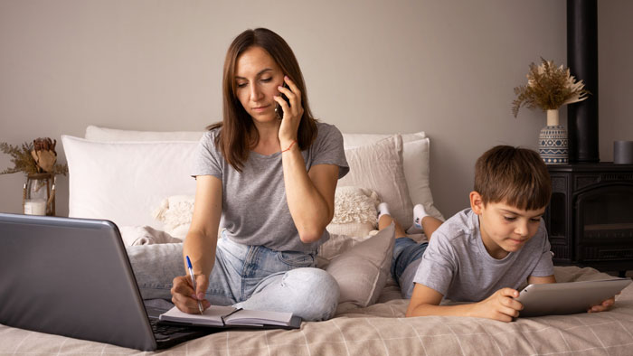 Teen helping with babysitting half siblings while mother talks on phone and works on laptop in cozy bedroom. Teen helping with babysitting half siblings while mother talks on phone and works on laptop in cozy bedroom.