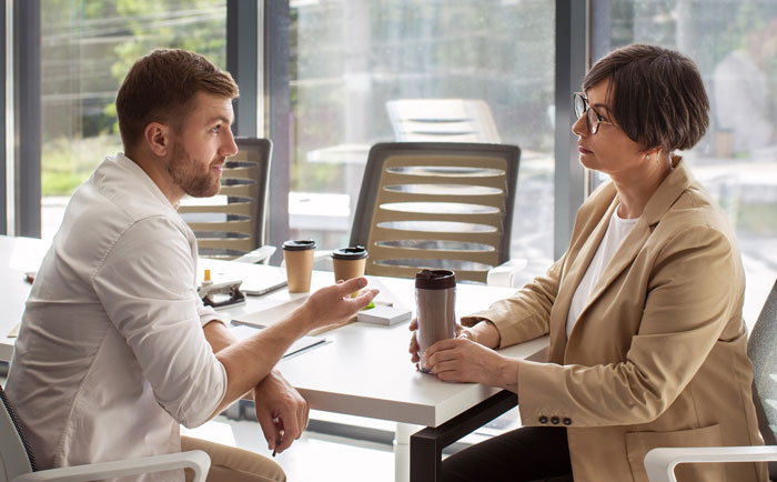 Man and woman having a serious discussion in office while woman holds a travel tumbler during a Tenerife vacation debate. Man and woman having a serious discussion in office while woman holds a travel tumbler during a Tenerife vacation debate.