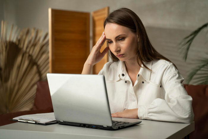 Woman working on laptop at home, appearing stressed as her Tenerife vacay is blocked by boss over focus concerns. Woman working on laptop at home, appearing stressed as her Tenerife vacay is blocked by boss over focus concerns.