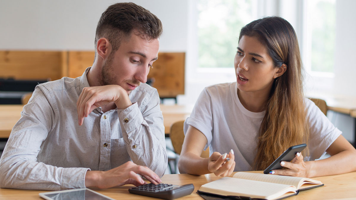 Couple having a tense discussion at table as husband uses calculator prioritizing luxury vehicle over family plans.