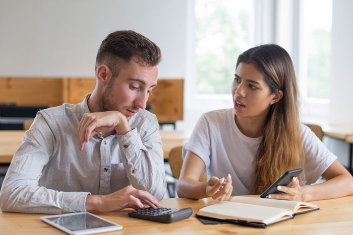 Couple arguing while using a calculator and phone, discussing priorities between luxury vehicle and family plans. Couple arguing while using a calculator and phone, discussing priorities between luxury vehicle and family plans.