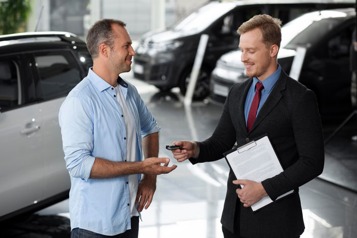 Man in casual wear receiving luxury vehicle keys from salesman in a dealership, highlighting hubby prioritizes luxury vehicle over family plans. Man in casual wear receiving luxury vehicle keys from salesman in a dealership, highlighting hubby prioritizes luxury vehicle over family plans.