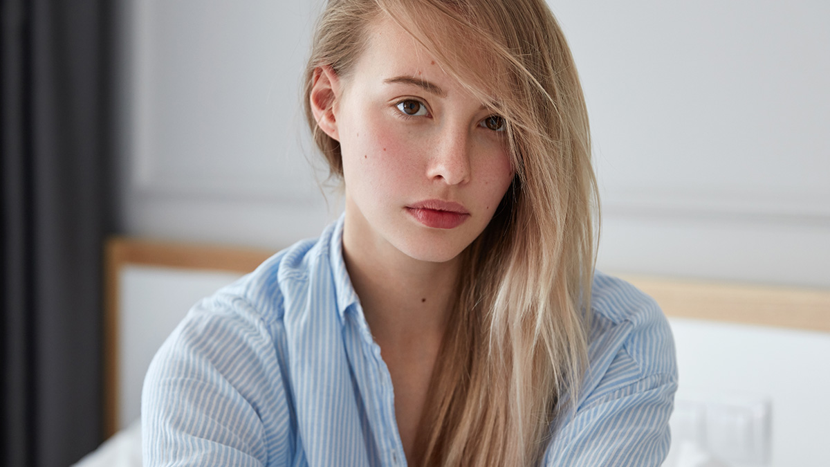 Young woman with a serious expression, wearing a blue striped shirt, reflecting on darkest family secrets discovered.