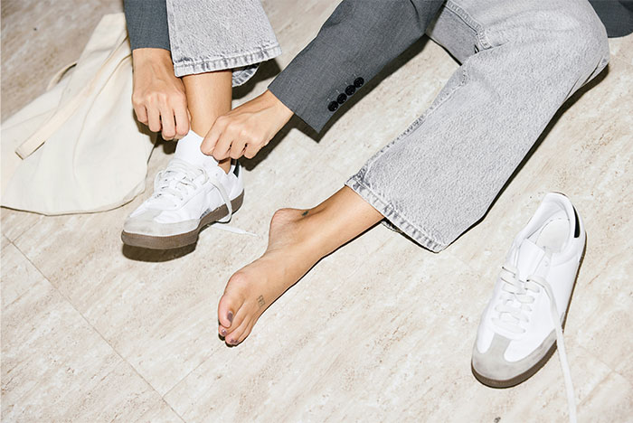 Person sitting on floor tying one sneaker while the other foot is bare, illustrating ways people got permanently banned from a friend's house.