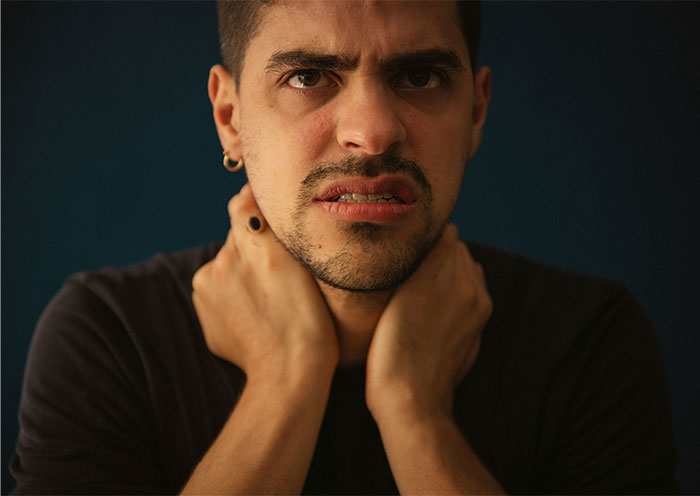 Young man distressed and anxious, clutching his neck, illustrating people banned from a friend’s house.