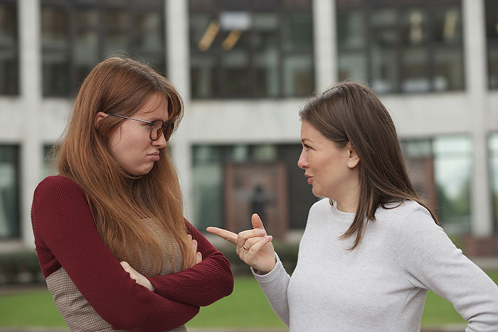 Two women outside a building in a heated conversation about money and family struggles.