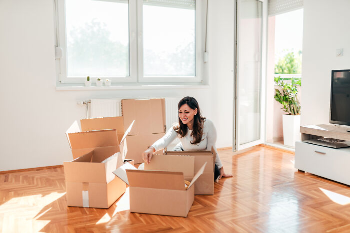 Woman sitting on floor unpacking cardboard boxes in a bright room, illustrating people sharing things they would never admit in real life.