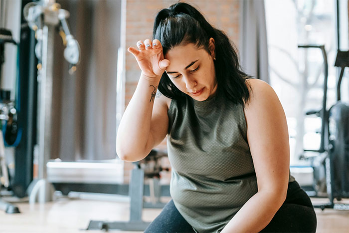 Overweight woman at gym looking distressed, reflecting on childhood trauma amid teens' laughter around her. Overweight woman at gym looking distressed, reflecting on childhood trauma amid teens' laughter around her.