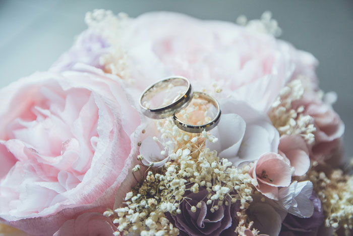 Two wedding rings resting on pink and white flowers representing a couple’s wedding sabotage before ceremony.