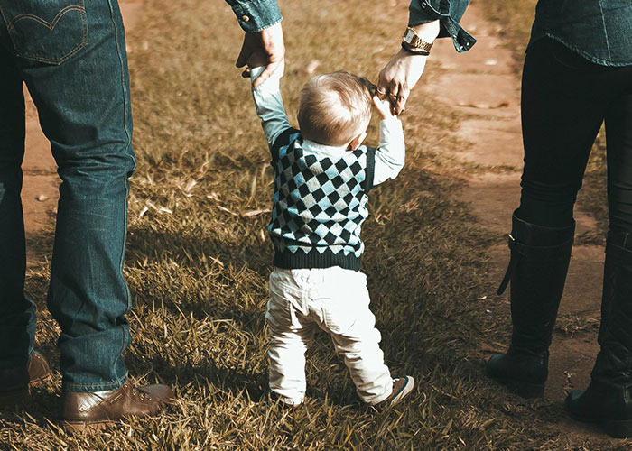 Toddler walking with parents holding hands on a grassy path, highlighting a story about illegal baby adoption and CPS report.