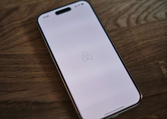 Smartphone displaying Airbnb app on wooden table, related to family rushes out of rental house after discovery. Smartphone displaying Airbnb app on wooden table, related to family rushes out of rental house after discovery.