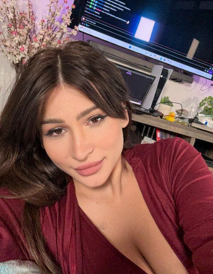 Young woman giving birth on Twitch livestream shown in a cozy room with computer screens and flowers in the background. Young woman giving birth on Twitch livestream shown in a cozy room with computer screens and flowers in the background.