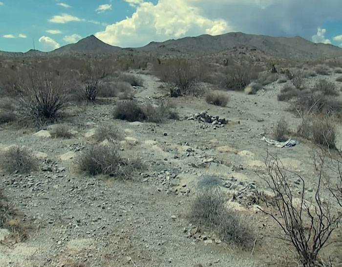 Dry Las Vegas desert landscape with scattered piles of human remains and sparse vegetation under a cloudy sky. Dry Las Vegas desert landscape with scattered piles of human remains and sparse vegetation under a cloudy sky.