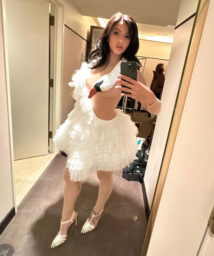 Pop star taking a mirror selfie in a white feather-inspired dress at Paris Fashion Week, showcasing dyed armpit hair. Pop star taking a mirror selfie in a white feather-inspired dress at Paris Fashion Week, showcasing dyed armpit hair.
