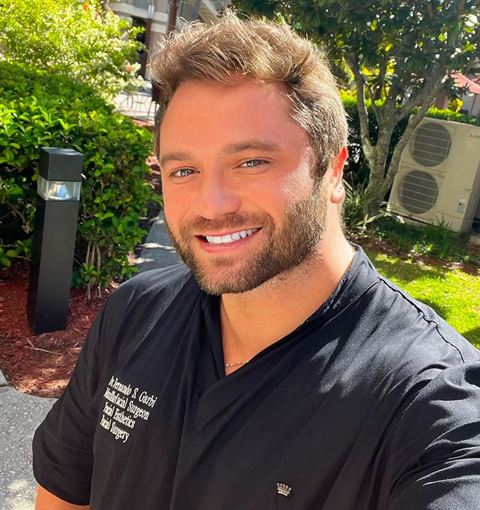 Smiling man outdoors wearing black shirt with text about facial surgeon, related to fox eyes surgery complications. Smiling man outdoors wearing black shirt with text about facial surgeon, related to fox eyes surgery complications.