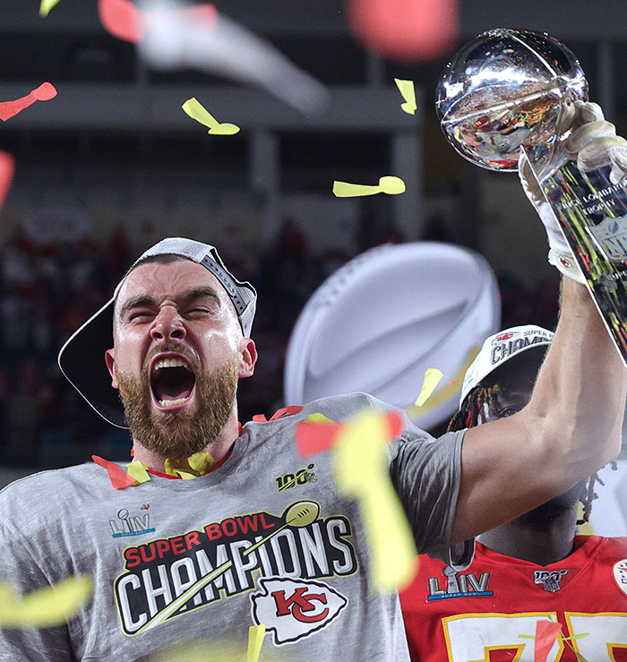 Travis Kelce celebrating Super Bowl victory holding trophy with confetti, linked to Taylor Swift fans and tradwife controversy. Travis Kelce celebrating Super Bowl victory holding trophy with confetti, linked to Taylor Swift fans and tradwife controversy.