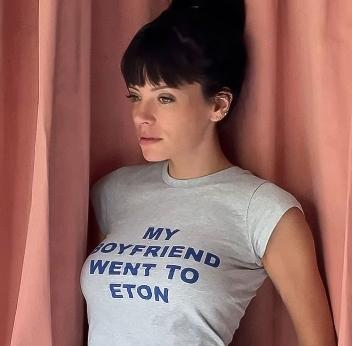 Woman wearing a t-shirt standing by pink curtains, related to fans clash online over David Harbour cheating controversy. Woman wearing a t-shirt standing by pink curtains, related to fans clash online over David Harbour cheating controversy.