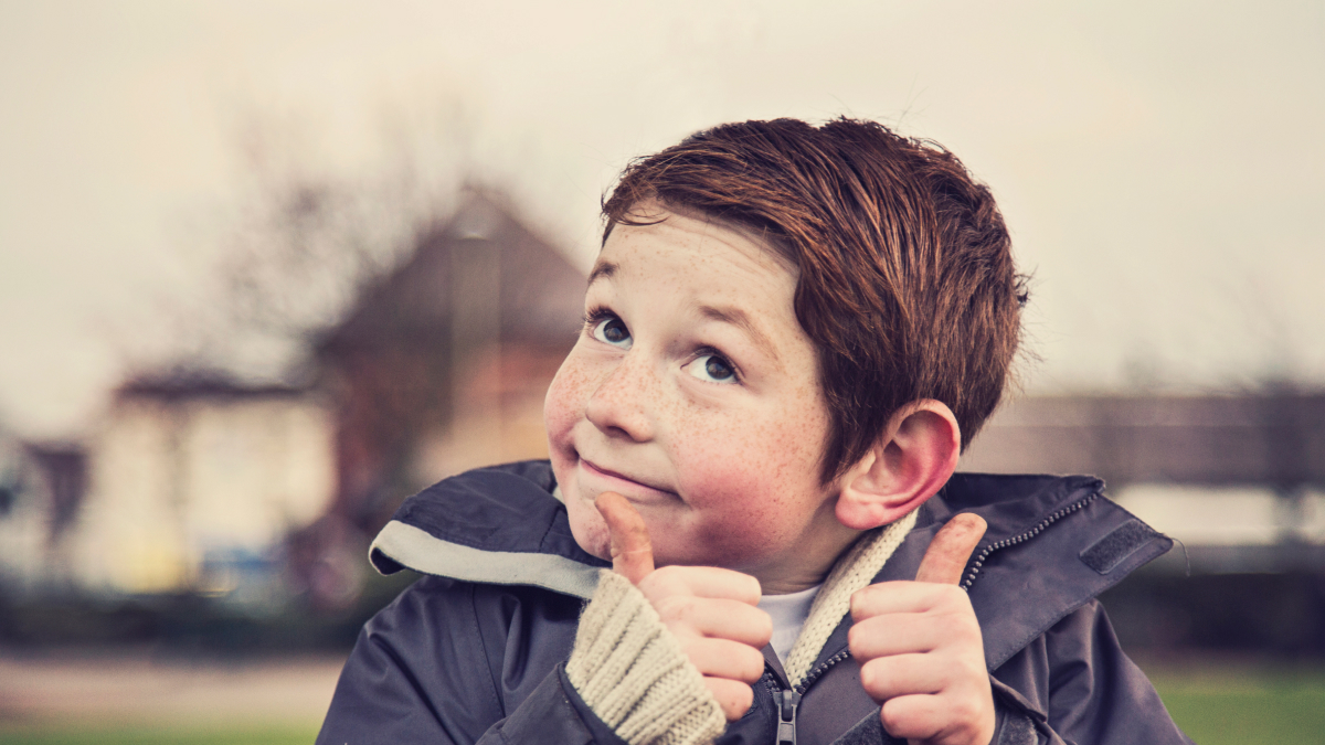 Young boy giving thumbs up with a funny expression outdoors, illustrating humorous responses to how are you questions.