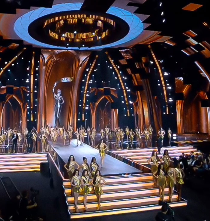 Miss Panama onstage during a beauty pageant, wearing a gold dress amid other contestants in a dramatic runway setting. Miss Panama onstage during a beauty pageant, wearing a gold dress amid other contestants in a dramatic runway setting.