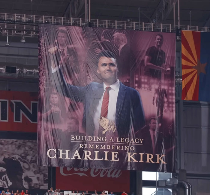 Large banner of Charlie Kirk in a suit and red tie inside a stadium, related to a controversial homework assignment. Large banner of Charlie Kirk in a suit and red tie inside a stadium, related to a controversial homework assignment.
