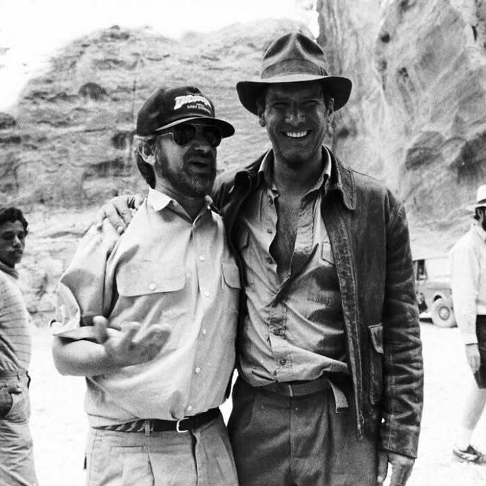 Two iconic figures from movie and music industries smiling together on a film set in a desert landscape. Two iconic figures from movie and music industries smiling together on a film set in a desert landscape.