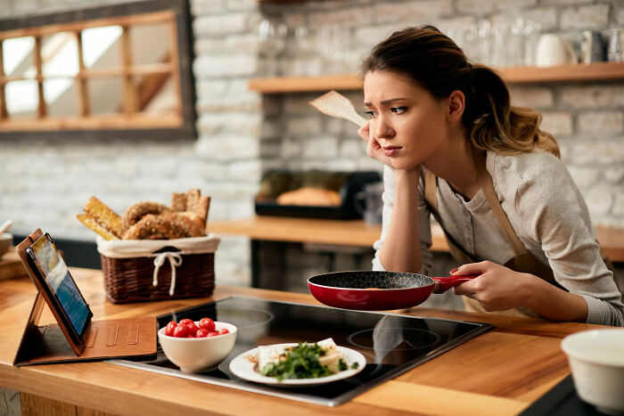 Woman looking distressed while cooking in kitchen, depicting unfair relationships due to traditional gender roles.