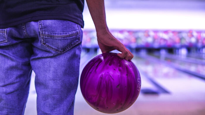 Person holding a purple bowling ball preparing to roll in a bowling alley, capturing a moment of anticipation and focus.