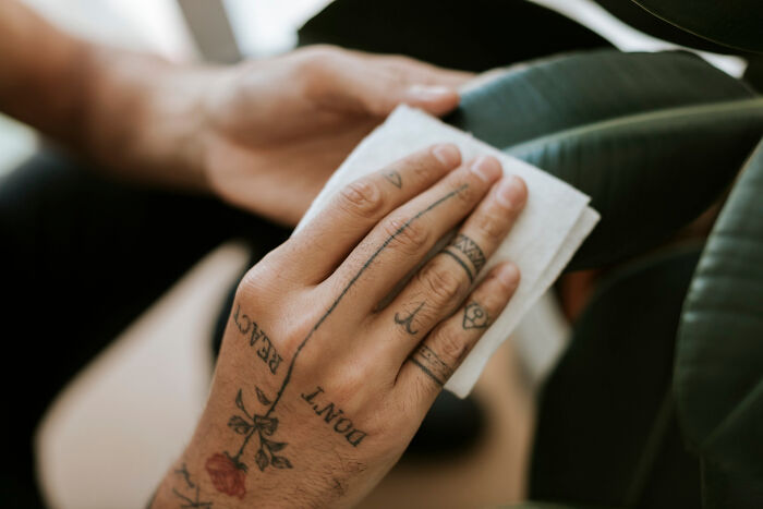 Close-up of a hand with tattoos cleaning a plant leaf, illustrating strange and offensive tattoo artists refusing to ink on people.