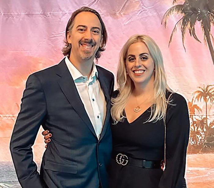 A smiling couple dressed formally posing in front of a tropical backdrop at an event related to breeding propaganda backlash. A smiling couple dressed formally posing in front of a tropical backdrop at an event related to breeding propaganda backlash.