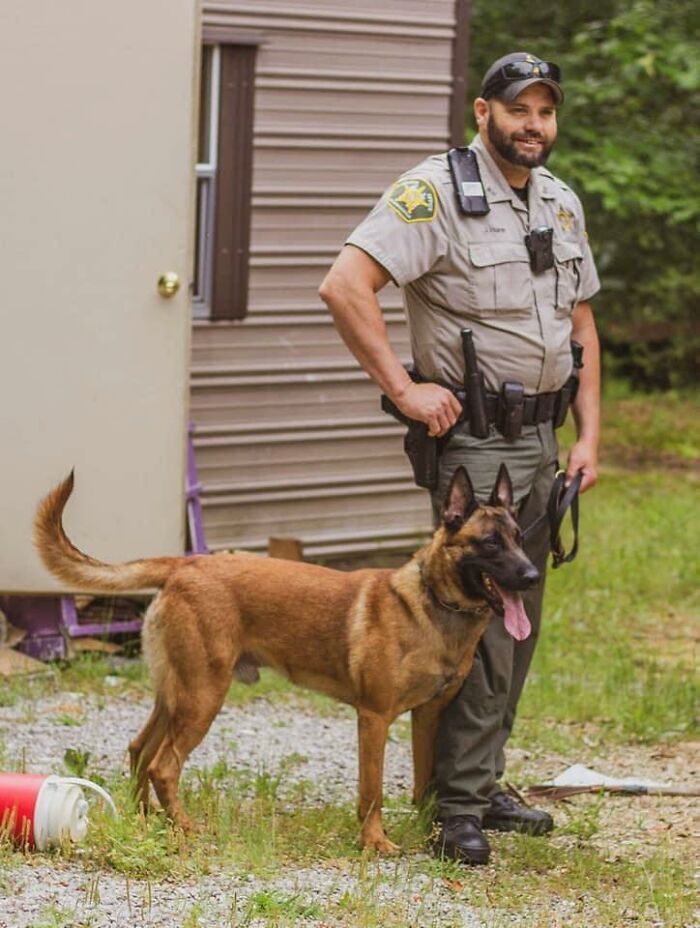 Police officer standing outdoors with a K9 unit dog near a building in a rural area. Police officer standing outdoors with a K9 unit dog near a building in a rural area.