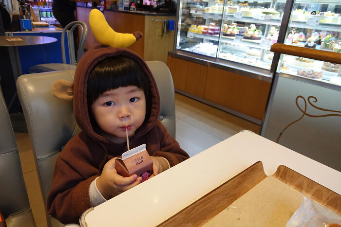 Child in a banana costume sipping a drink at a restaurant, illustrating tales from restaurant staff about the bill and money issues.