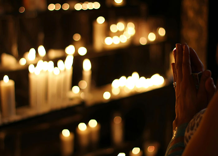Person praying with hands clasped near lit candles, symbolizing reflection on mental health myths debunked by psychologists.