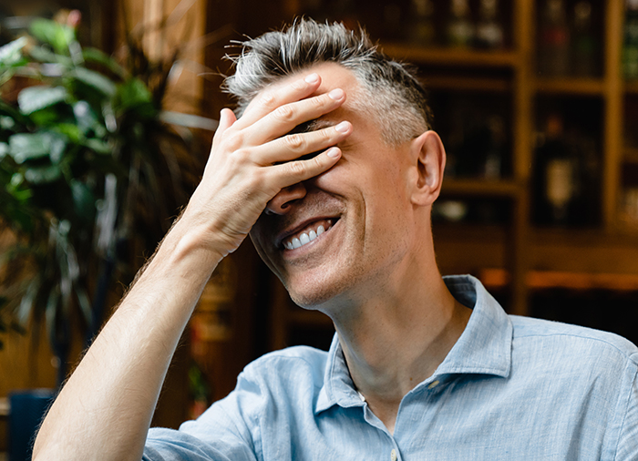 Man in a blue shirt smiling and covering his face, conveying embarrassment amid spicy chicken sandwich chaos. Man in a blue shirt smiling and covering his face, conveying embarrassment amid spicy chicken sandwich chaos.