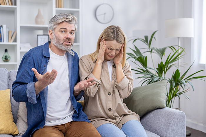 Middle-aged couple arguing on a couch with woman upset and man explaining, symbolizing golden child lost parents money crypto issue. Middle-aged couple arguing on a couch with woman upset and man explaining, symbolizing golden child lost parents money crypto issue.