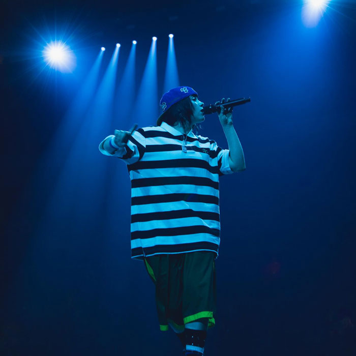 Billie Eilish performing on stage under blue lights during Miami concert with fans reacting to snatching attempt. Billie Eilish performing on stage under blue lights during Miami concert with fans reacting to snatching attempt.