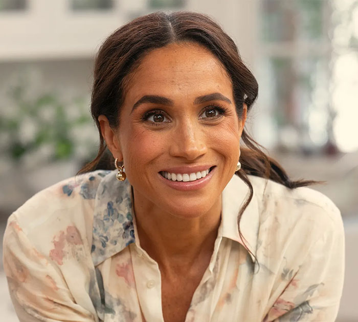 Meghan Markle smiling warmly indoors, wearing a floral blouse, related to Paris Fashion Week and Balenciaga designer. Meghan Markle smiling warmly indoors, wearing a floral blouse, related to Paris Fashion Week and Balenciaga designer.