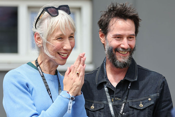 Keanu Reeves smiling with Alexandra Grant, both wearing lanyards, appearing happy and engaged in conversation outdoors. Keanu Reeves smiling with Alexandra Grant, both wearing lanyards, appearing happy and engaged in conversation outdoors.