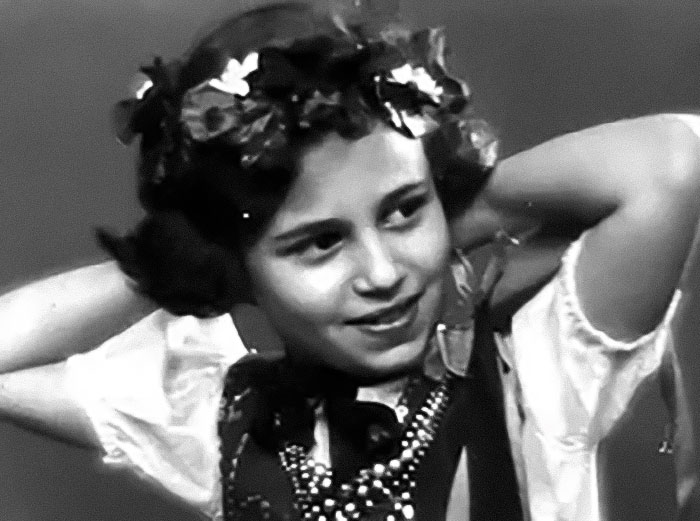 Black and white photo of Holocaust survivor Ruth Posner as a young girl wearing a floral headband and traditional clothing. Black and white photo of Holocaust survivor Ruth Posner as a young girl wearing a floral headband and traditional clothing.
