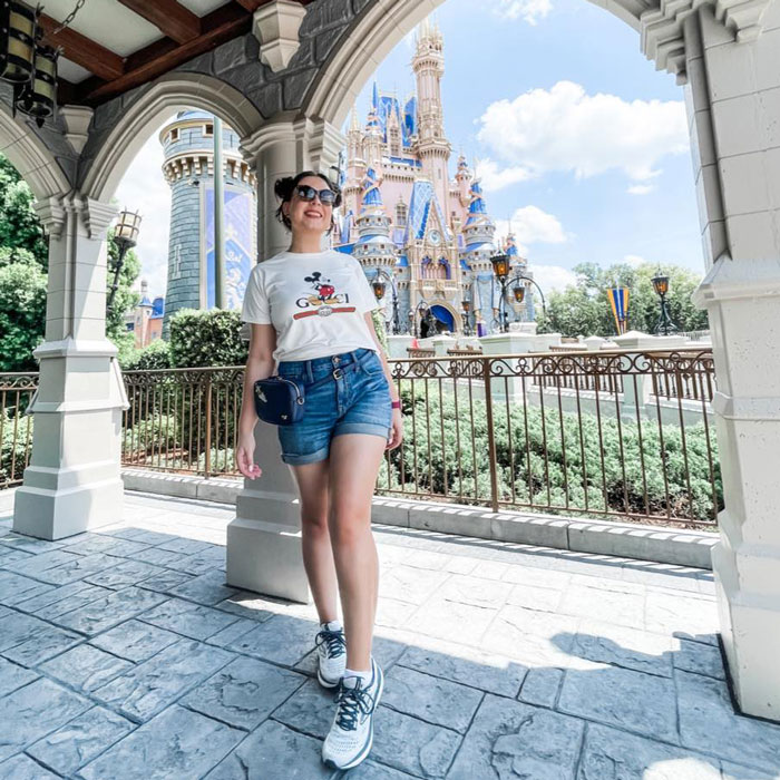 Pregnant Disney superfan posing in sunglasses and shorts near a castle at a Disney theme park on a sunny day. Pregnant Disney superfan posing in sunglasses and shorts near a castle at a Disney theme park on a sunny day.