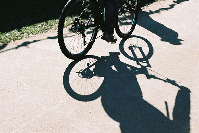 Shadow of a person riding a bicycle on pavement, illustrating a woman knocked unconscious by bird insurance claim denied. Shadow of a person riding a bicycle on pavement, illustrating a woman knocked unconscious by bird insurance claim denied.