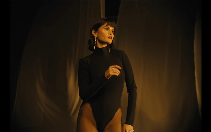 Selena Gomez posing in a dark bodysuit with dramatic lighting, sparking discussion about her face in new music video. Selena Gomez posing in a dark bodysuit with dramatic lighting, sparking discussion about her face in new music video.