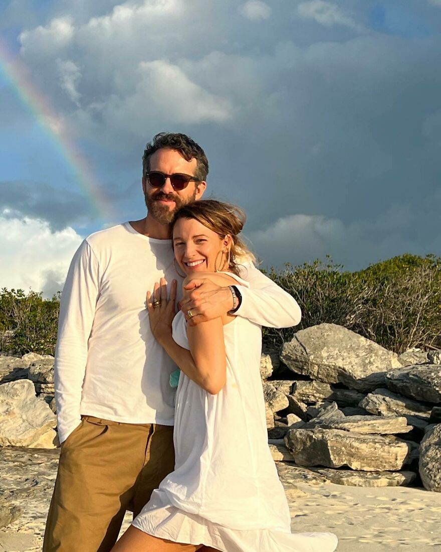 Ryan Reynolds And Blake Lively embracing outdoors on rocky beach with a rainbow, representing Hollywood’s most enduring power couples.