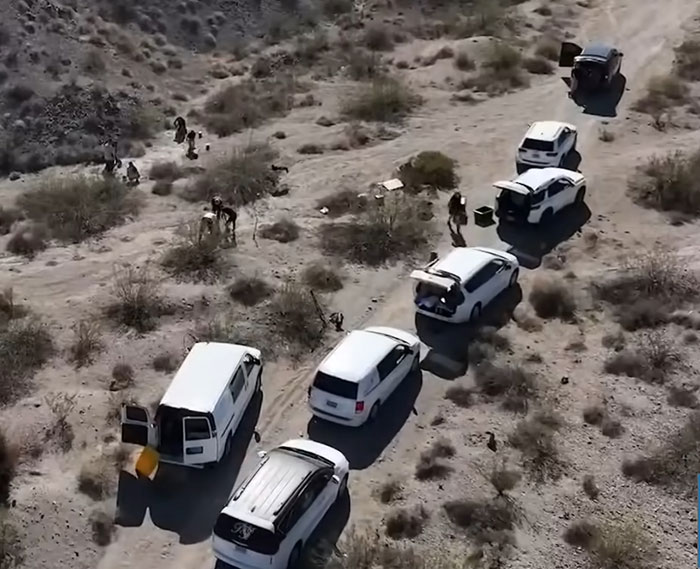 Aerial view of urgent investigation at Las Vegas desert with multiple vehicles and people examining piles of human remains. Aerial view of urgent investigation at Las Vegas desert with multiple vehicles and people examining piles of human remains.