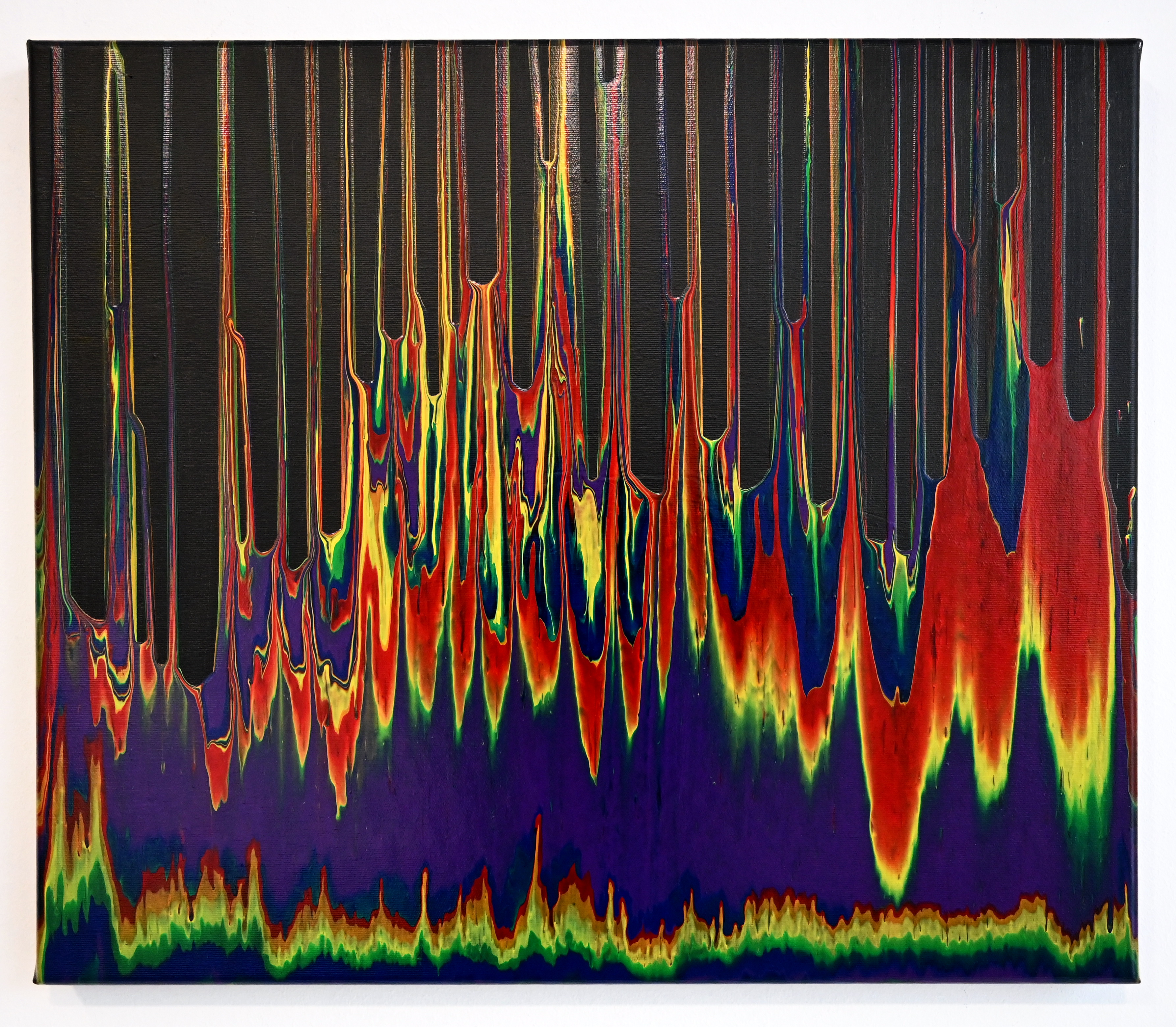 Gravity flow acrylic pour painting featuring vibrant rainbow colors cascading vertically on a black canvas background.