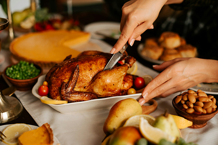 Woman carving Thanksgiving turkey at festive table with classic side dishes in warm holiday setting Woman carving Thanksgiving turkey at festive table with classic side dishes in warm holiday setting