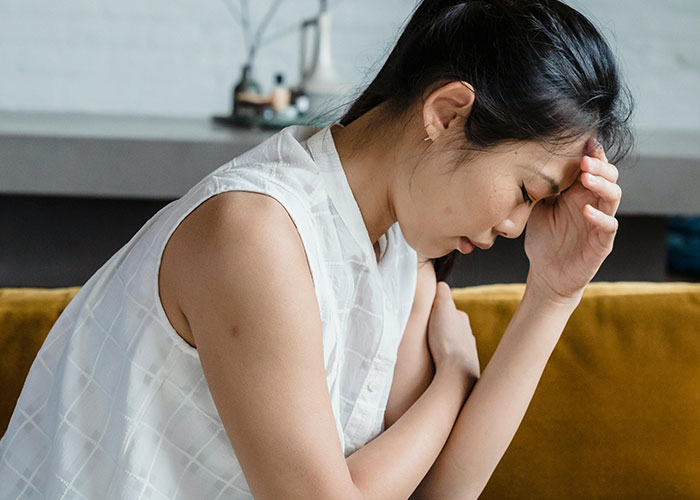 Young woman sitting on a couch, holding her head in distress, illustrating mental health myths and psychological challenges.