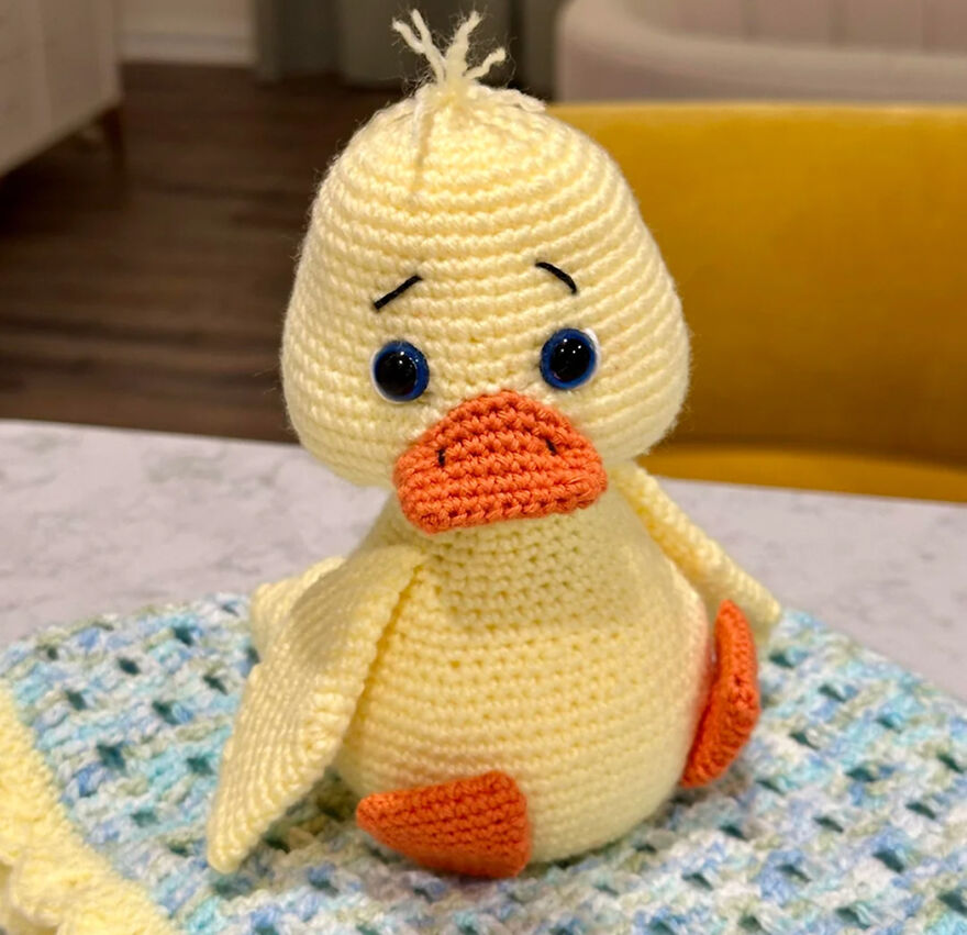 Crochet animal duck with big eyes and an expressive face sitting on a handmade textured blanket indoors.