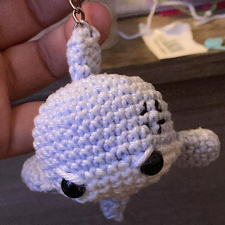 Hand holding a small crochet animal keychain shaped like a white seal with black eyes and stitched facial features.